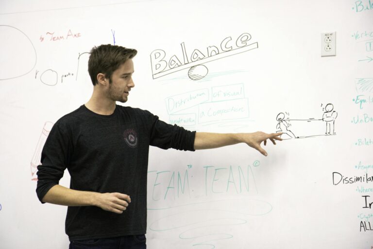 A young adult explaining concepts using a whiteboard in a classroom setting.